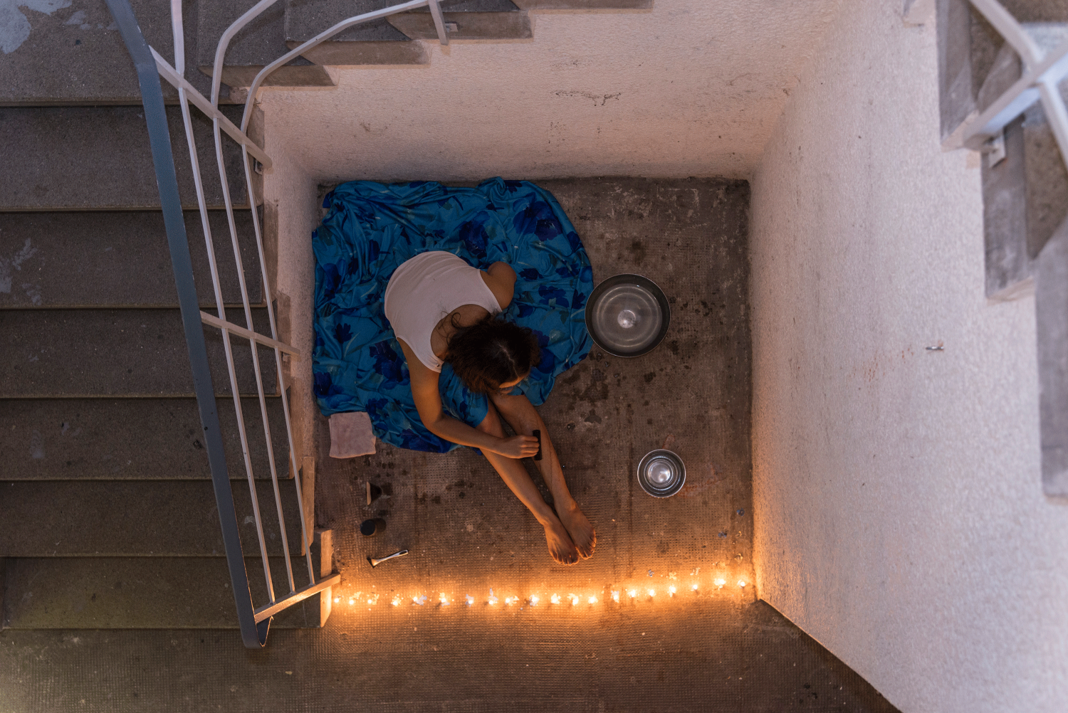 Das Foto zeigt die Performerin Therese Friedemann. Sie sitzt im Treffenhaus des Leerstandes, trägt einen blauen Rock und rasiert sich die Beine.