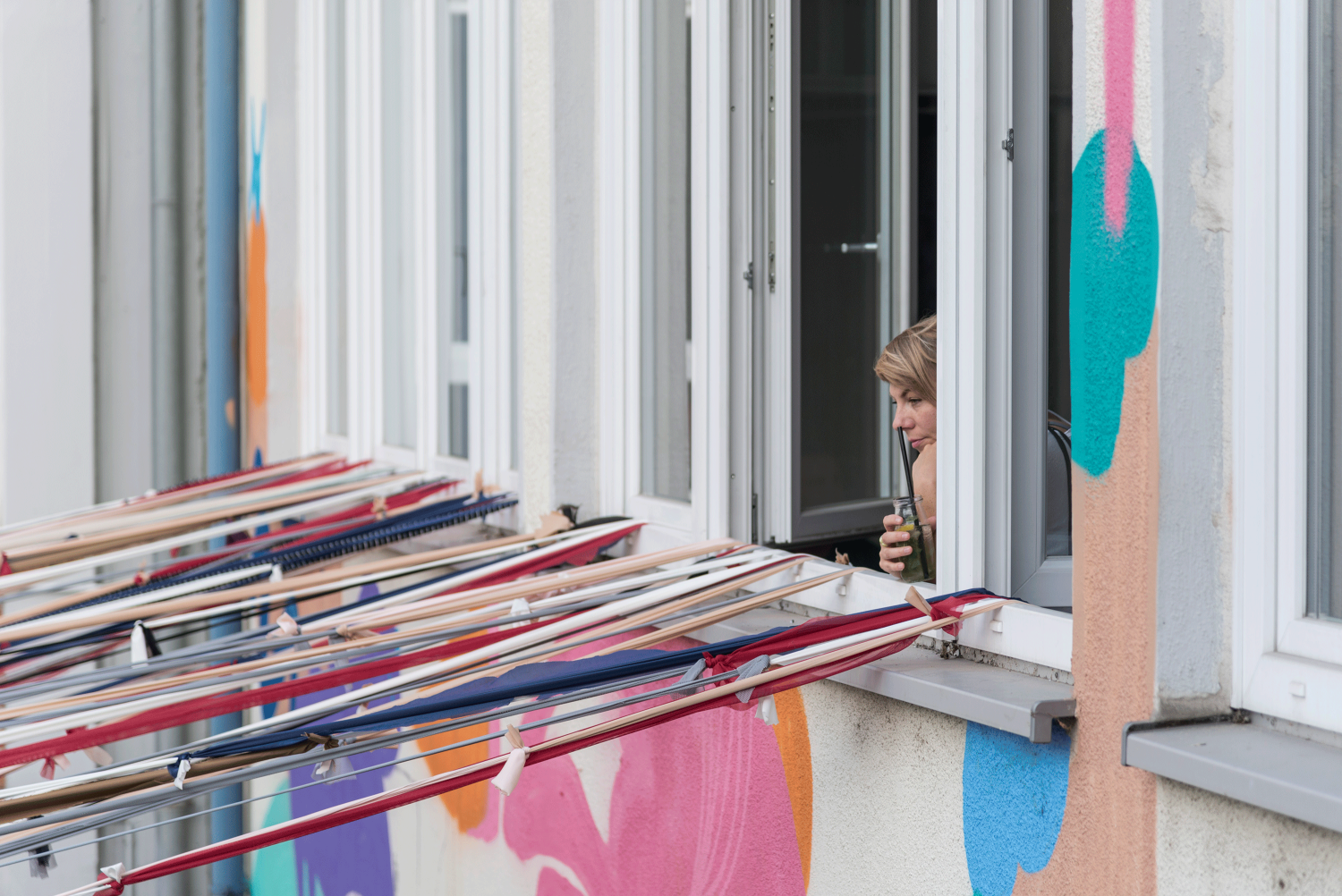 Zu sehen ist die Fassade der Manufaktur, die Fenster sind geöffnet und eine Person mit einem Drink in der Hand schaut aus dem Fenster.